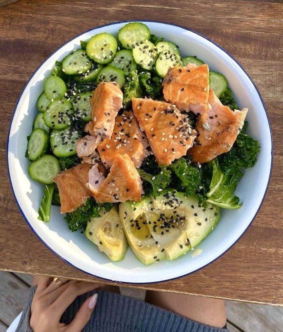 a bowl of salmon and cucumber salad with sesame seeds on the side is being held up by someone's hand