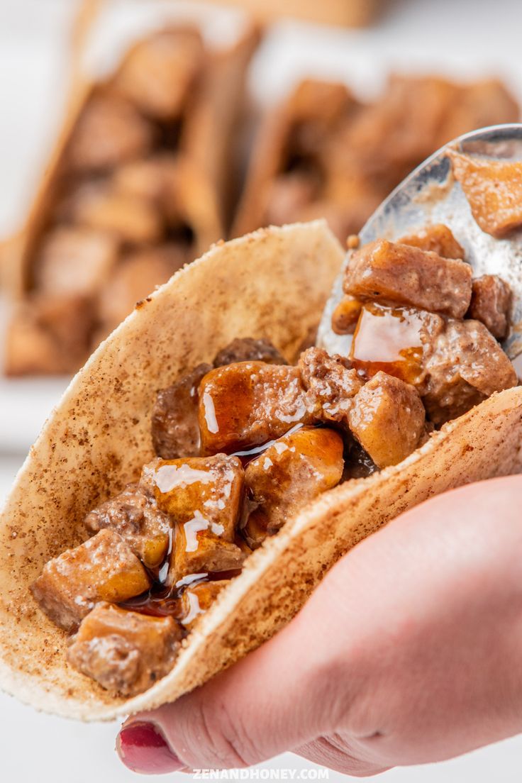 a hand holding a taco filled with meat and sauce