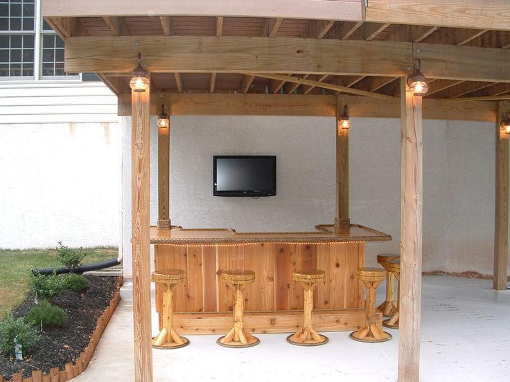 an outdoor bar with stools and a television mounted on the wall above it in a backyard