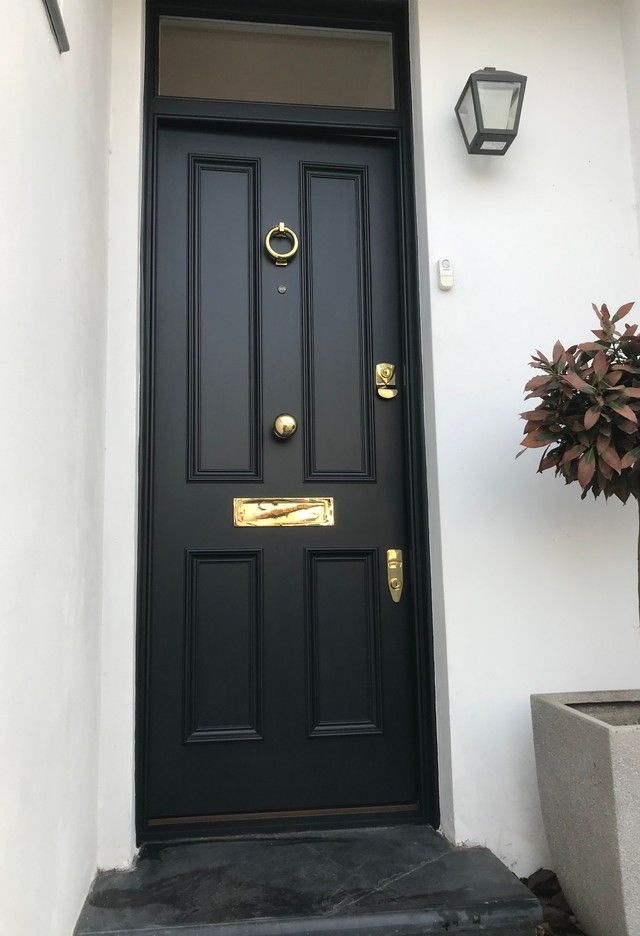 a black front door with gold handles on a white wall next to a potted plant