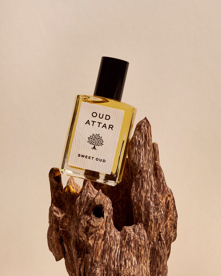 a bottle of oud attar sitting on top of a tree stump in front of a white background