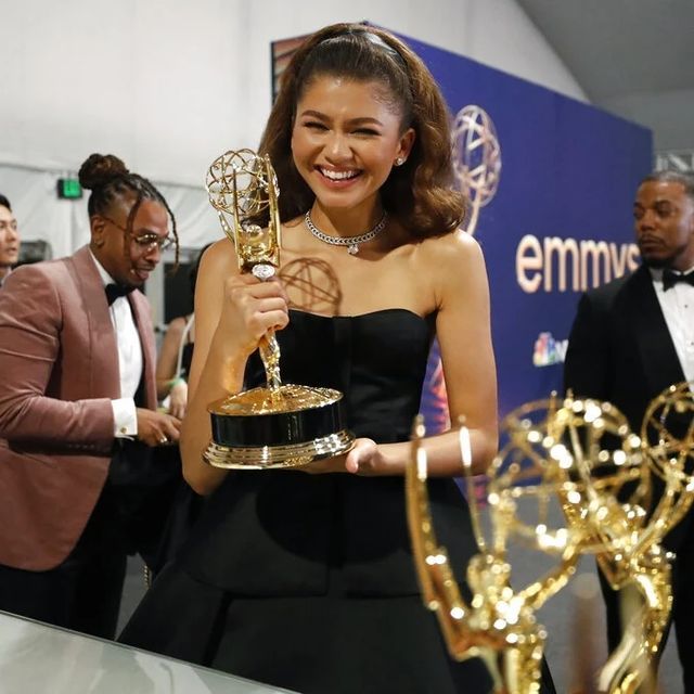 a woman holding an award in her hand and smiling at the camera while standing next to other people