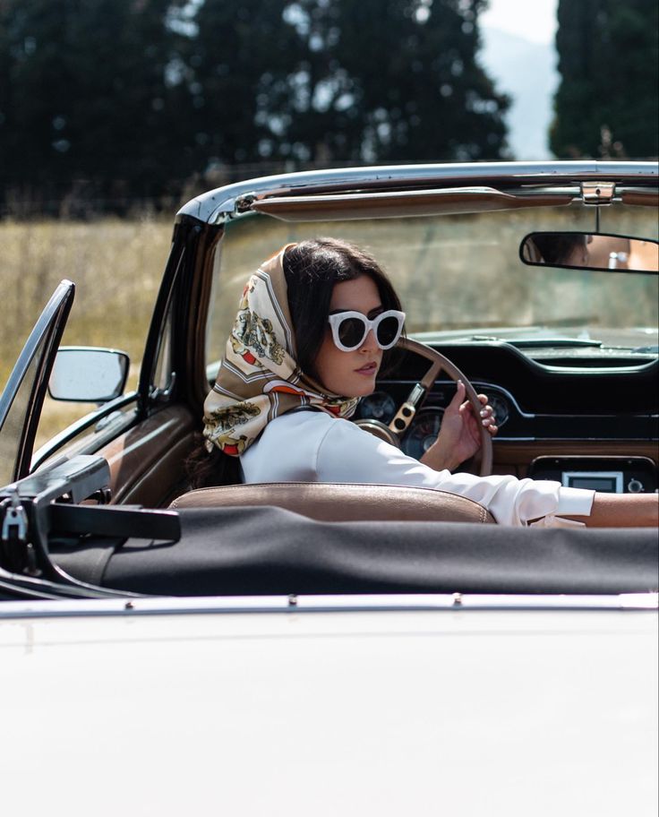 a woman sitting in the driver's seat of a car with a scarf on her head