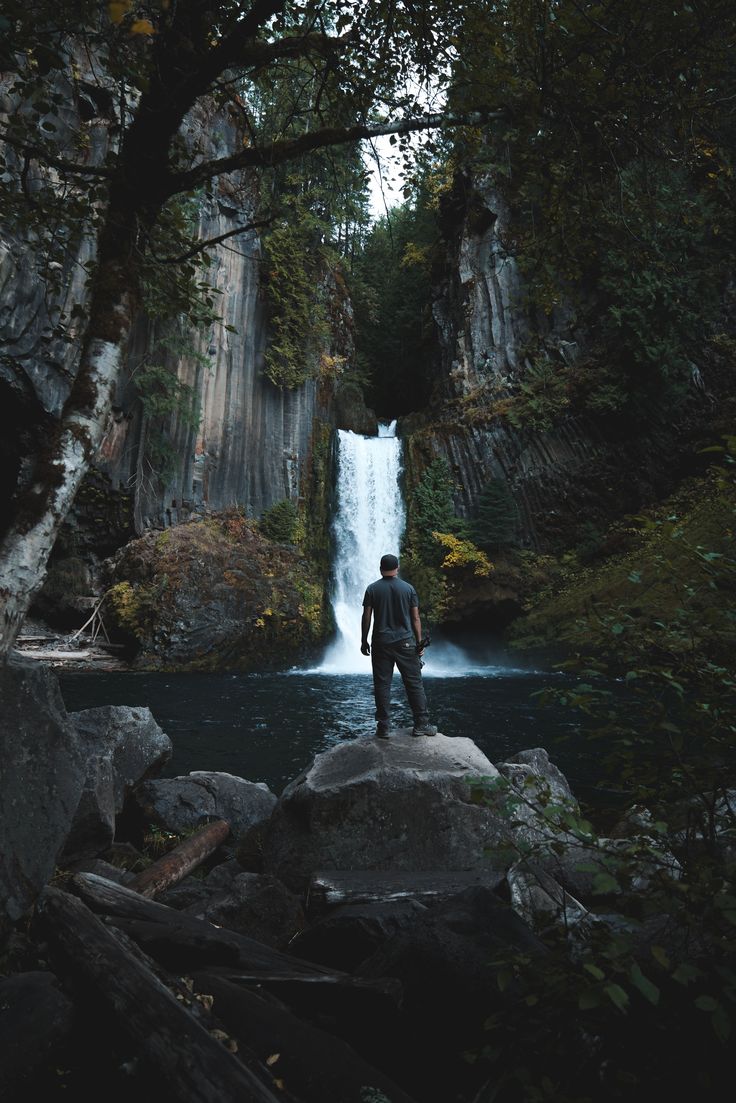 a man standing on rocks in front of a waterfall