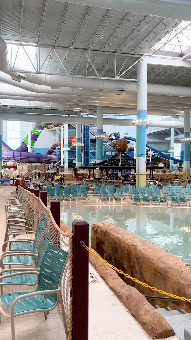 a large indoor swimming pool with lots of chairs around the perimeter and water slides in the background