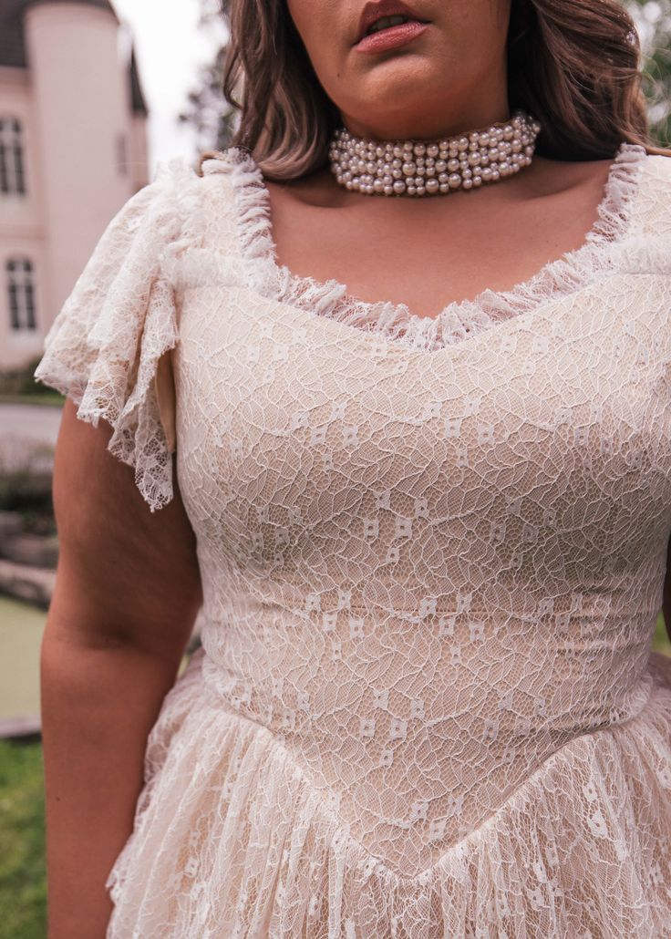 a woman in a white dress with a choker around her neck and pearls on the collar