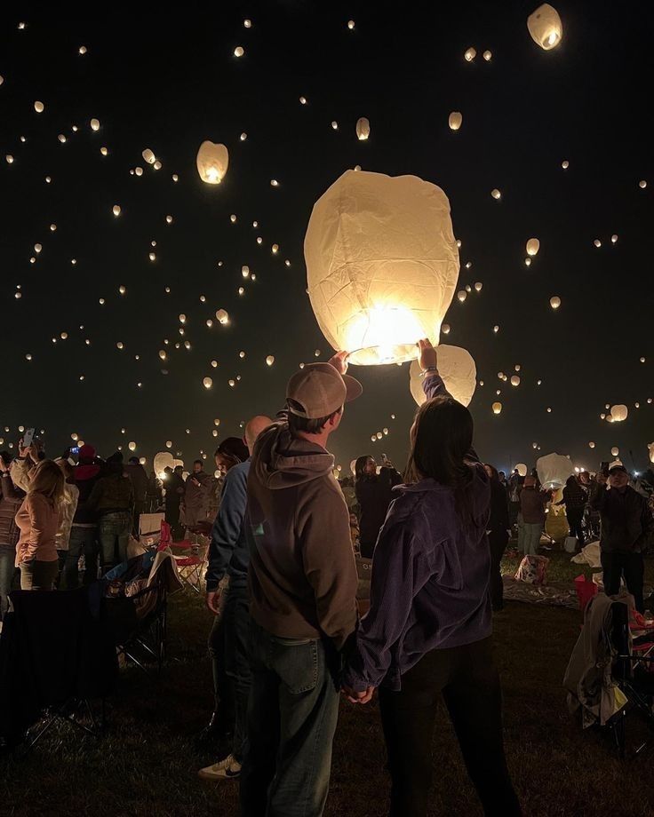 people are flying lanterns in the sky at night