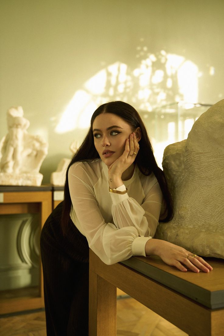 a woman is sitting on a bench with her hand near her face and looking at the camera