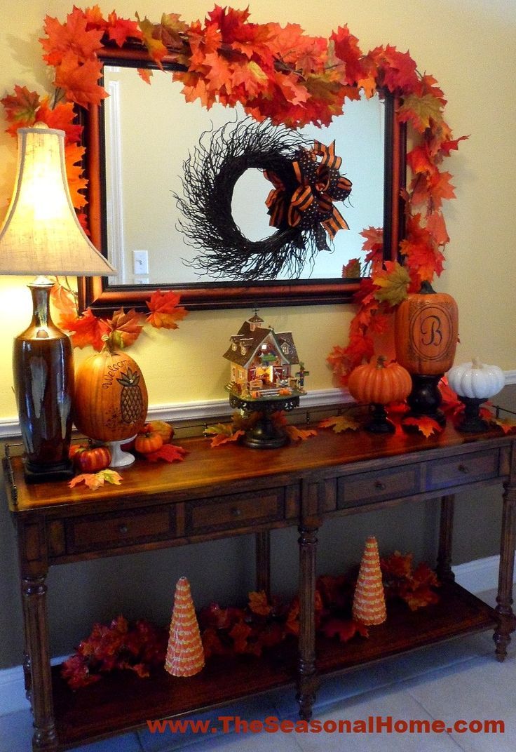 an entryway decorated for fall with pumpkins, leaves and a wreath on the table