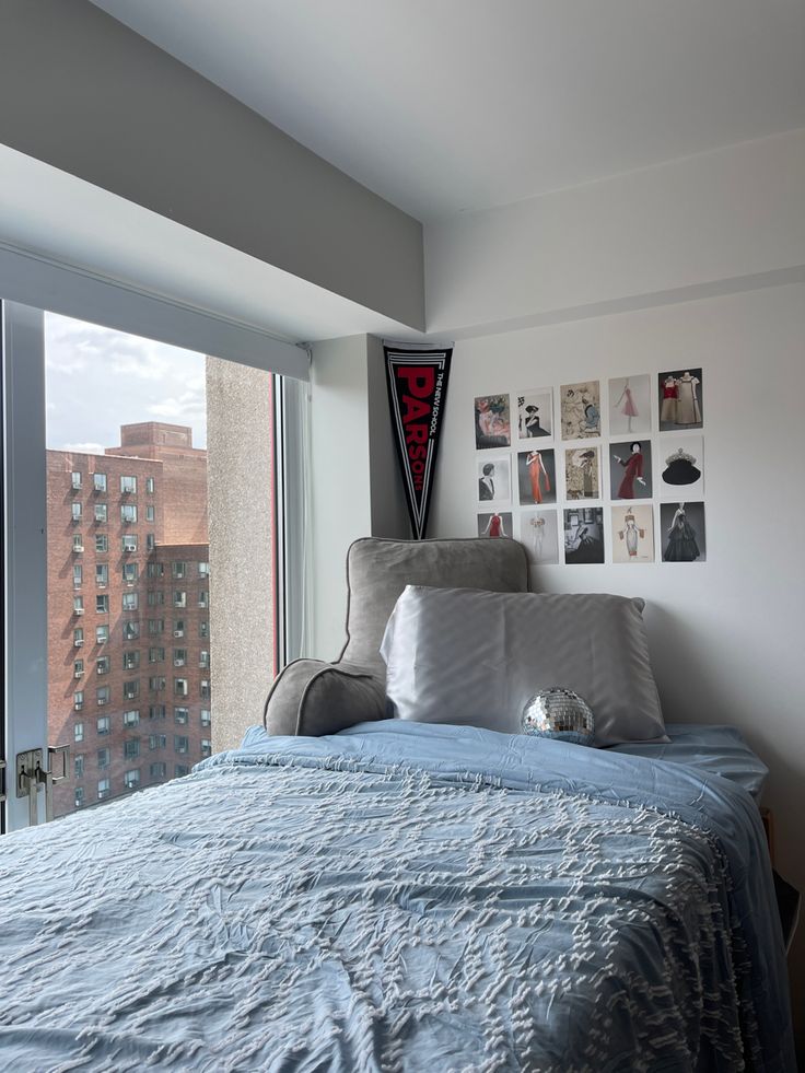 a bed with blue sheets and pillows in a bedroom next to a window overlooking the city