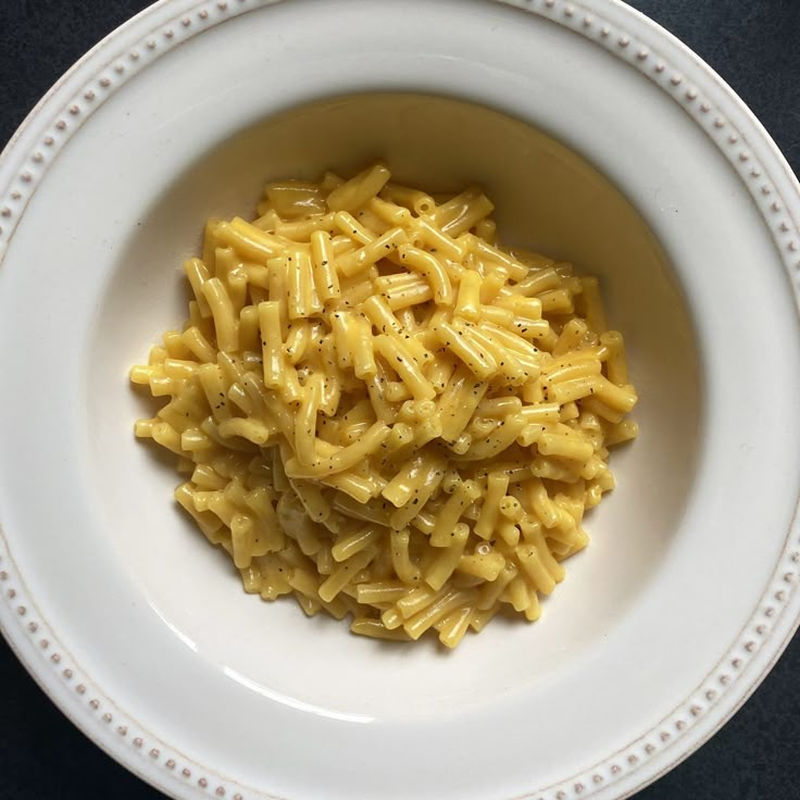 a white bowl filled with macaroni and cheese on top of a black table