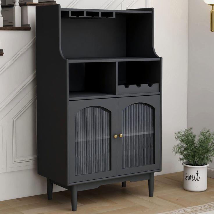 a black cabinet sitting on top of a wooden floor next to a potted plant