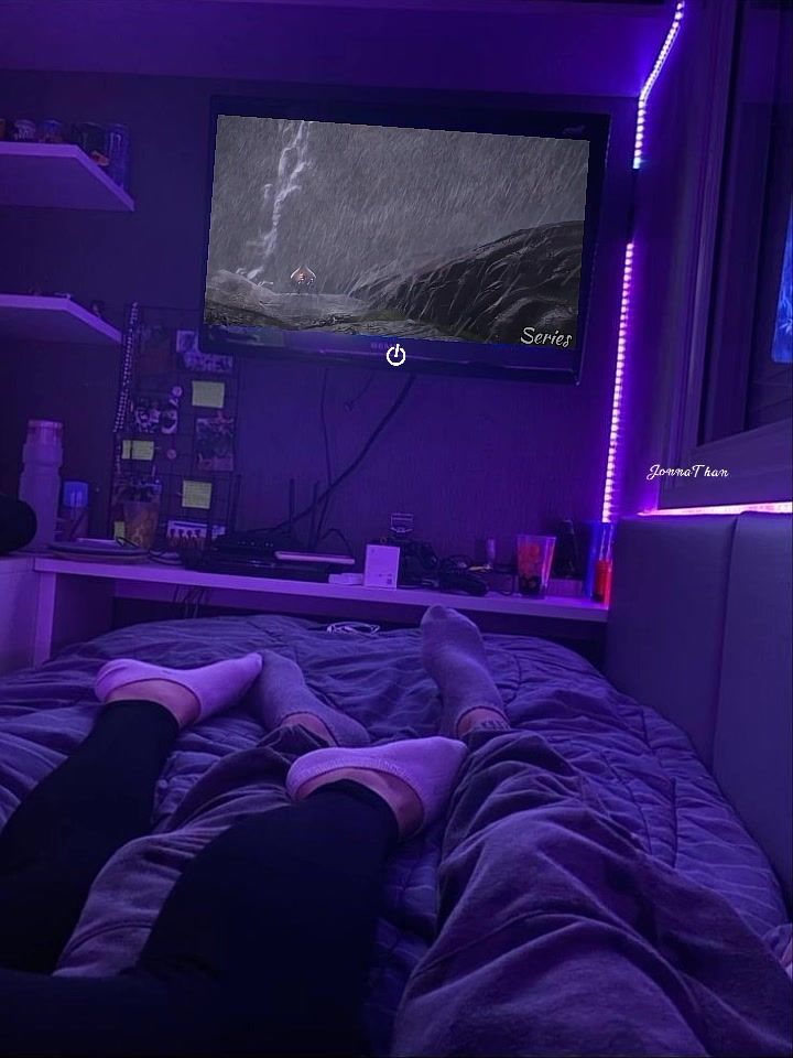 a person laying on a bed in front of a flat screen tv with purple lighting