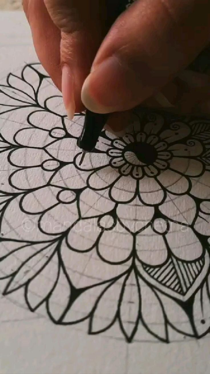 a person is drawing on paper with a pen and inking it into a flower design