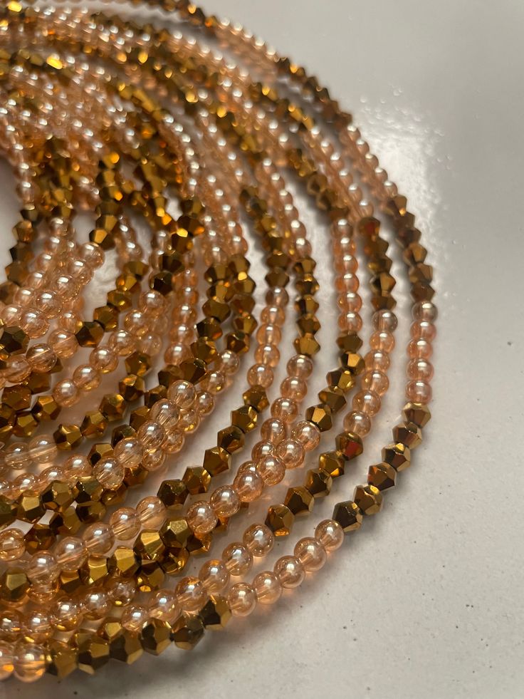 Elastic Waist Bead "Koun-Fao" crafted with resplendent gold glass crystal seed beads and adorned with delicate light brown glass seed bead accents. This elastic waist bead not only emanates opulence but also embodies a warm and earthy elegance, offering a comfortable and adjustable fit that transcends beauty and symbolism. 🌟 Gold Glass Crystal Seed Beads - Opulent Radiance: Koun-Fao is adorned with a luxurious array of gold glass crystal seed beads, creating an opulent radiance that symbolizes Elegant Gold Polished Waist Beads, Gold Waist Beads With Colorful Beads For Festivals, Bohemian Waist Beads With Spacer Beads For Party, Brown Gold Beads Jewelry For Party, Bohemian Waist Beads For Parties With Spacer Beads, Bohemian Beaded Waist Beads For Parties, Gold Round Waist Beads For Gifts, Elegant Gold Beads For Festival, Gold Copper Jewelry With Faceted Beads