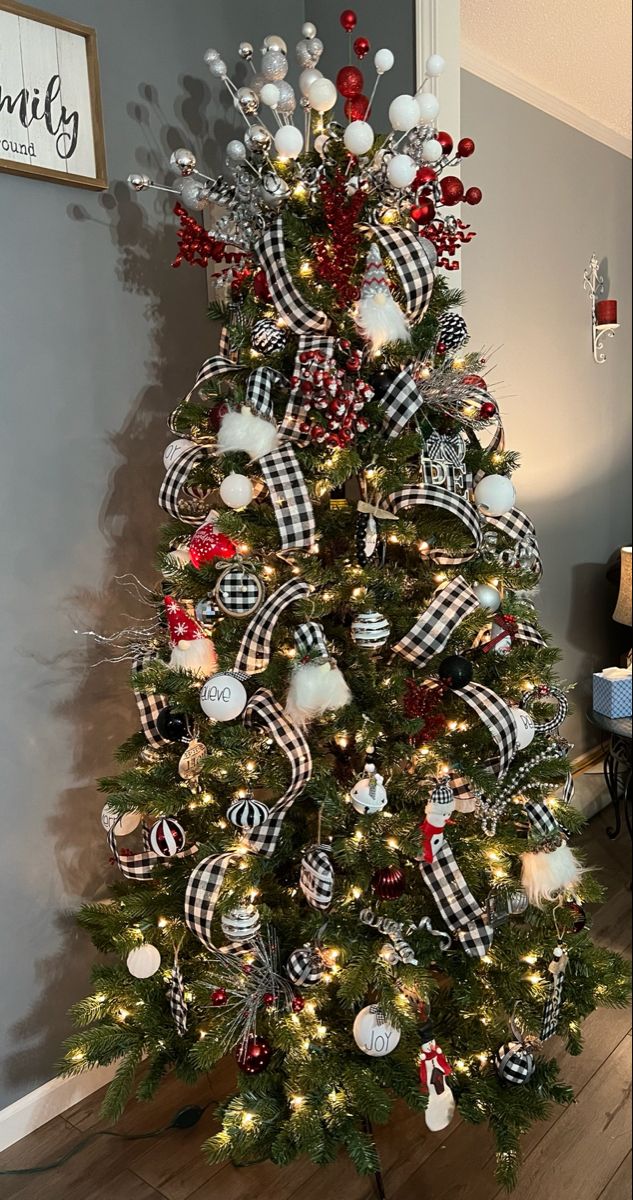 a christmas tree decorated with black and white plaid ribbon, ornaments and red bow on it