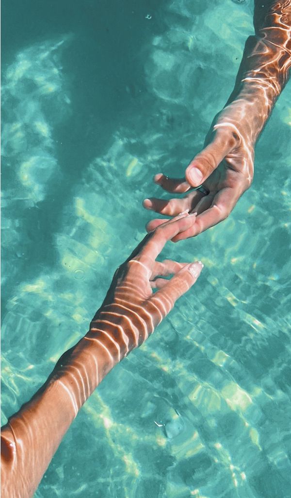 two people reaching out to touch each other in the blue water, with one person holding their hand