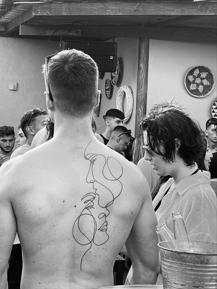 a man with a tattoo on his back standing in front of a group of people