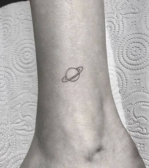 a small saturn tattoo on the ankle is shown in black and white, as well as an