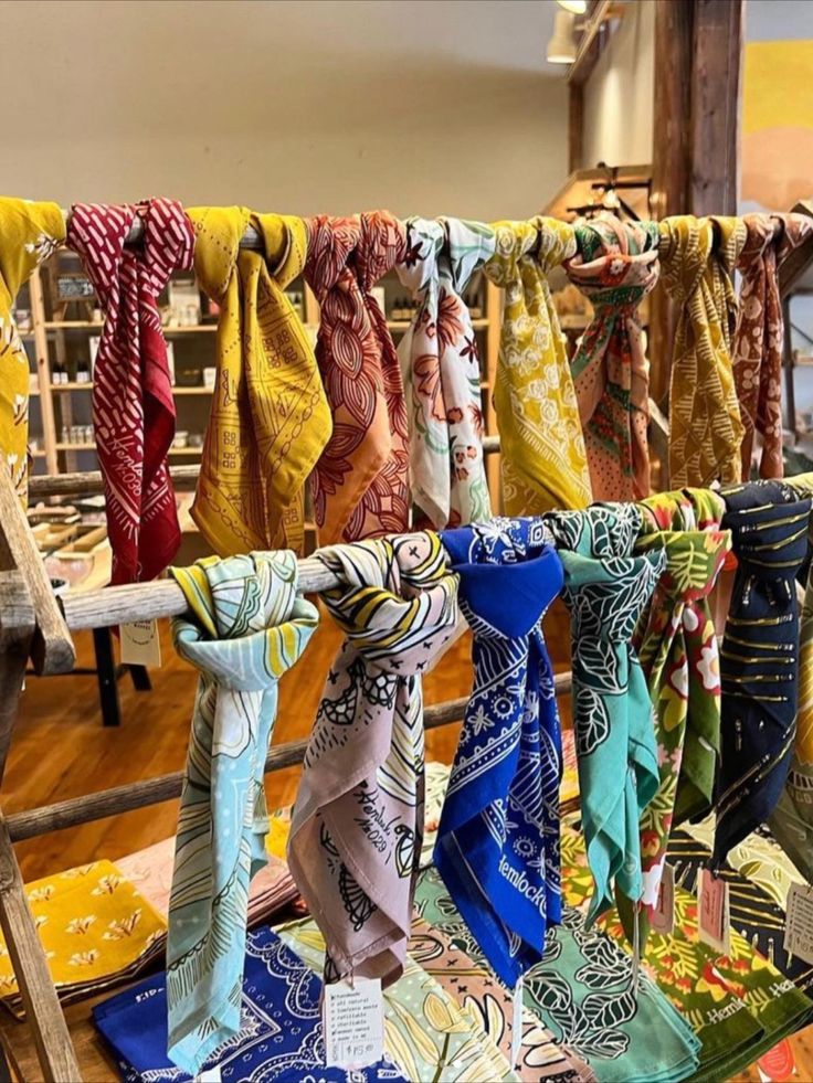 many different colored scarves are hanging on a clothes line in a store with wooden racks