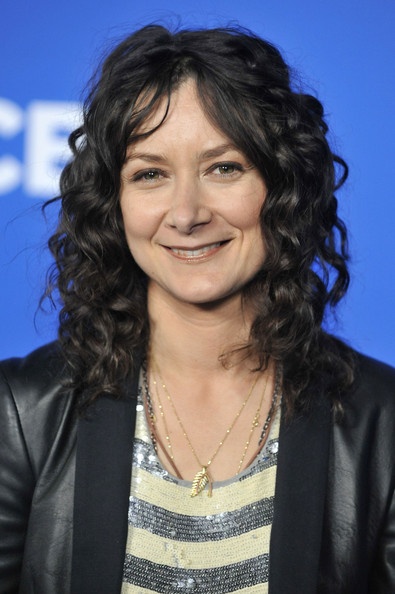 a woman with long curly hair smiles at the camera while standing in front of a blue backdrop