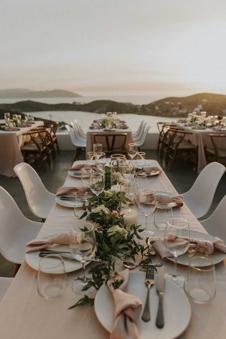 a long table is set with plates and place settings for an outdoor dinner party overlooking the ocean