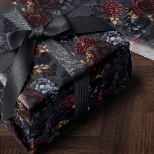 a gift wrapped in black and red floral paper with a bow on top, sitting on a wood floor