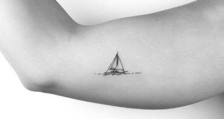 a black and white photo of a woman's arm with a small sailboat tattoo on it