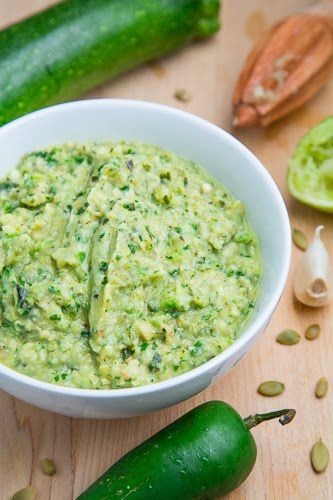 a white bowl filled with green sauce next to cucumbers