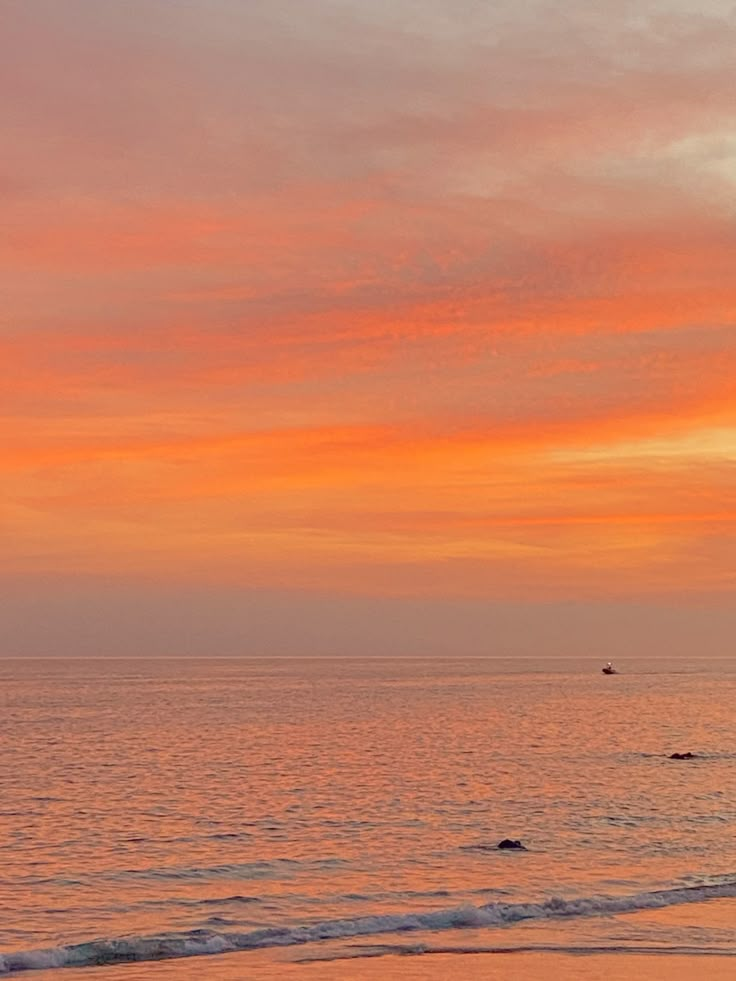 two people walking on the beach with surfboards under an orange and pink sky at sunset