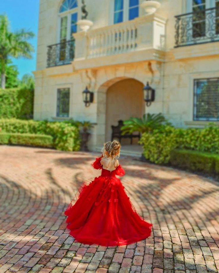 a woman in a red dress is standing on a brick walkway outside a large house