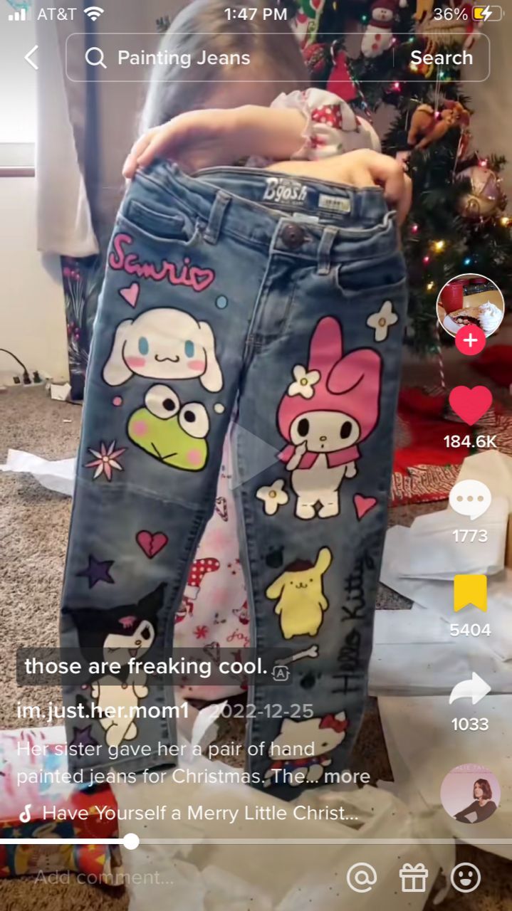 the girl is standing in front of her christmas tree wearing jeans with cartoon characters on them