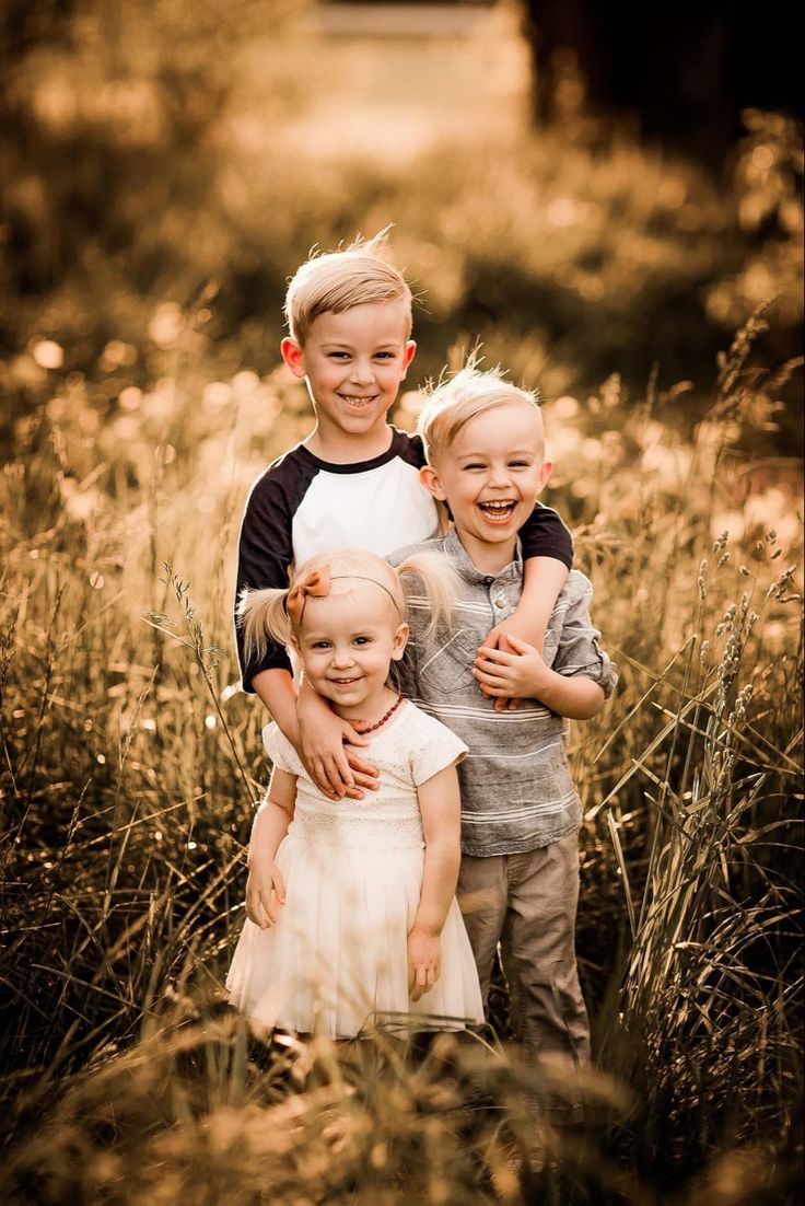 three young children standing in tall grass with their arms around each other