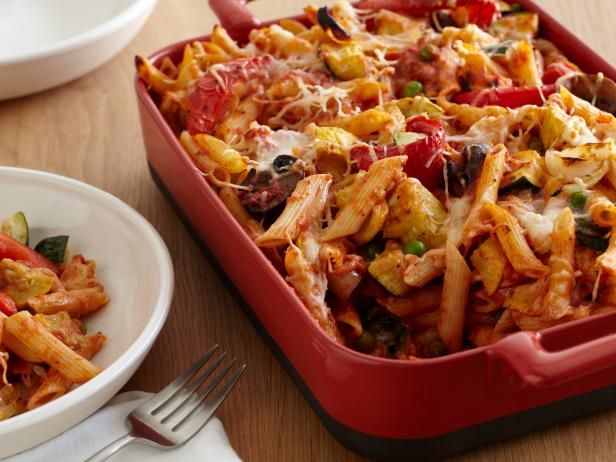 a red casserole dish filled with pasta and veggies on a wooden table