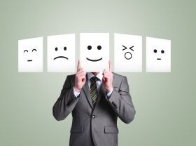 a man in a suit holding up four white cards with different faces drawn on them