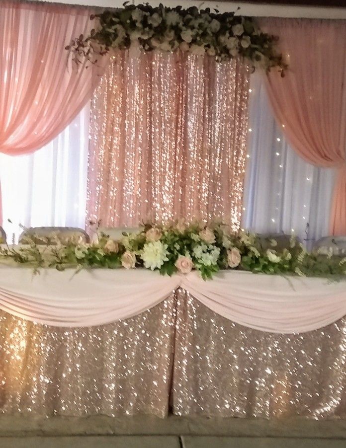 a table with flowers and greenery on it in front of a curtained window