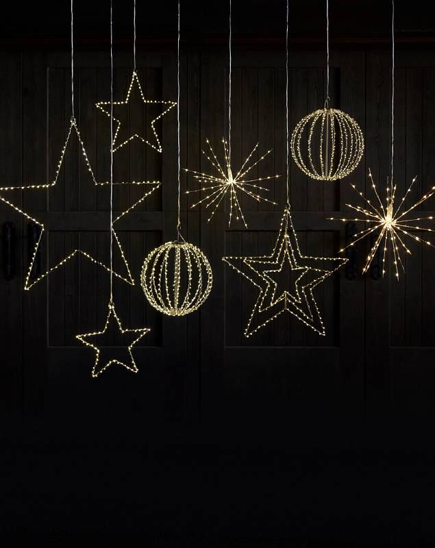 christmas lights hanging from the ceiling in front of a wooden wall with stars and balls