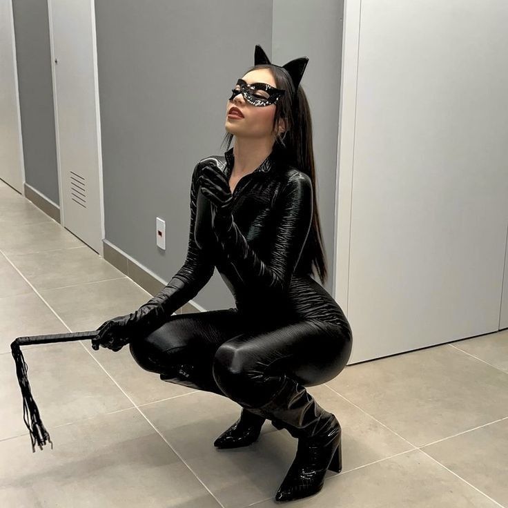 a woman in black catsuits is sitting on the floor