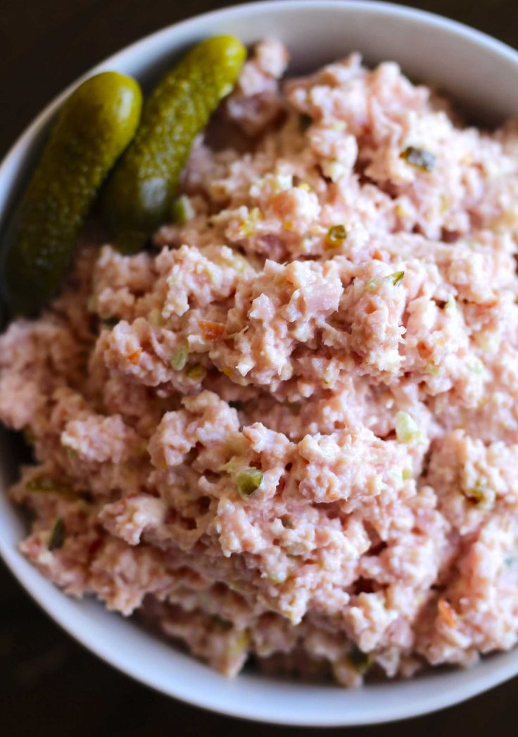 a white bowl filled with tuna salad next to a pickle