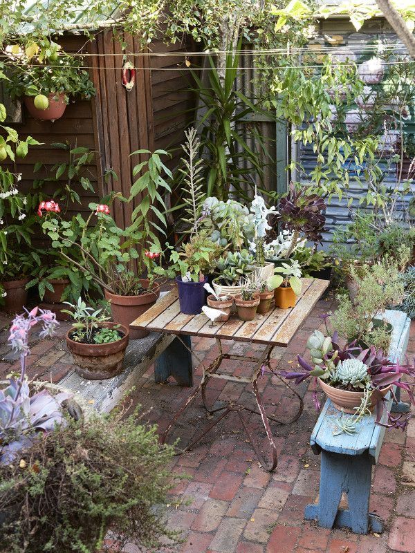 an outdoor table with potted plants on it in the middle of a garden area