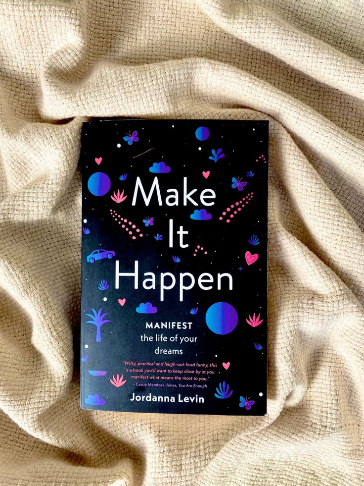 the book make it happen is laying on top of a white sheet with pink and blue designs