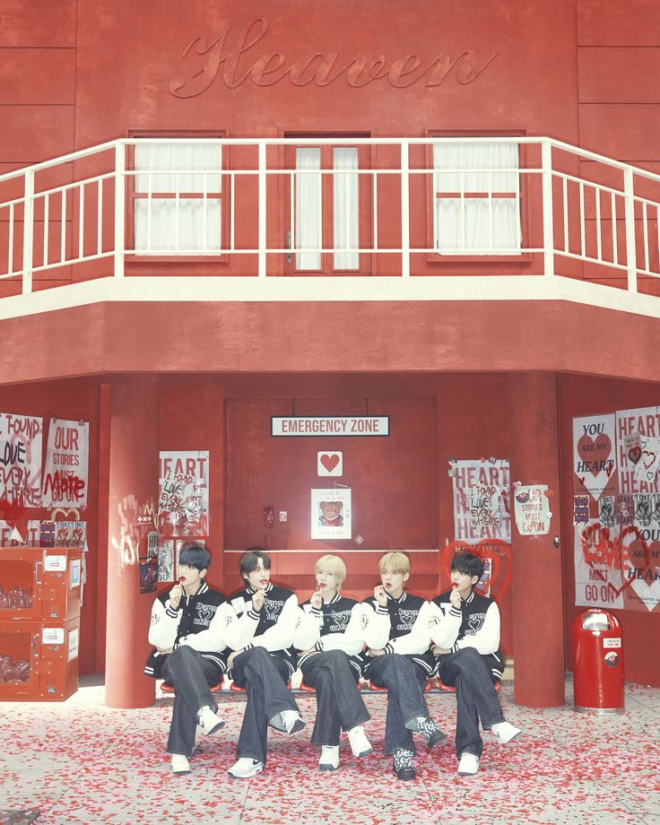 four people sitting on a bench in front of a red building