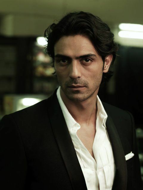 a man in a black suit and white shirt looking at the camera with serious expression on his face