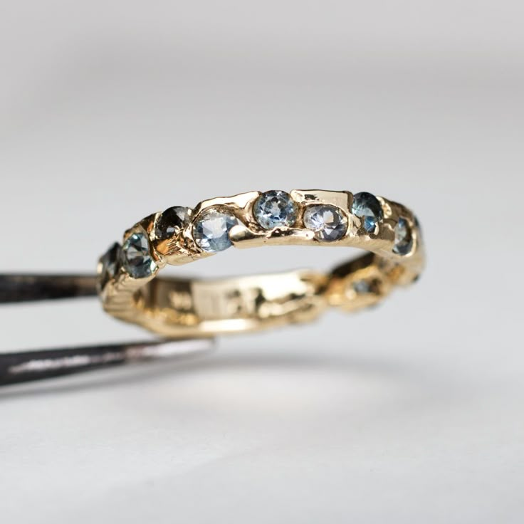 two gold wedding bands with blue and white diamonds on them, sitting next to each other