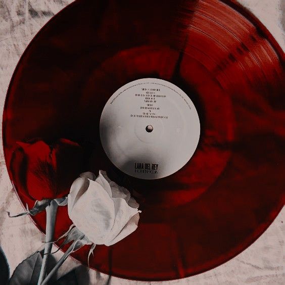 a red vinyl record sitting on top of a white cloth covered table next to a flower