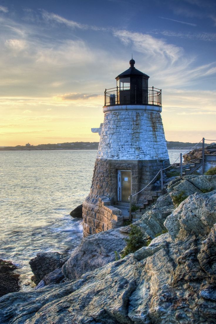 a light house sitting on top of a rocky cliff next to the ocean at sunset