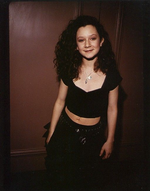 a woman standing in front of a wall with her hands on her hips and looking at the camera