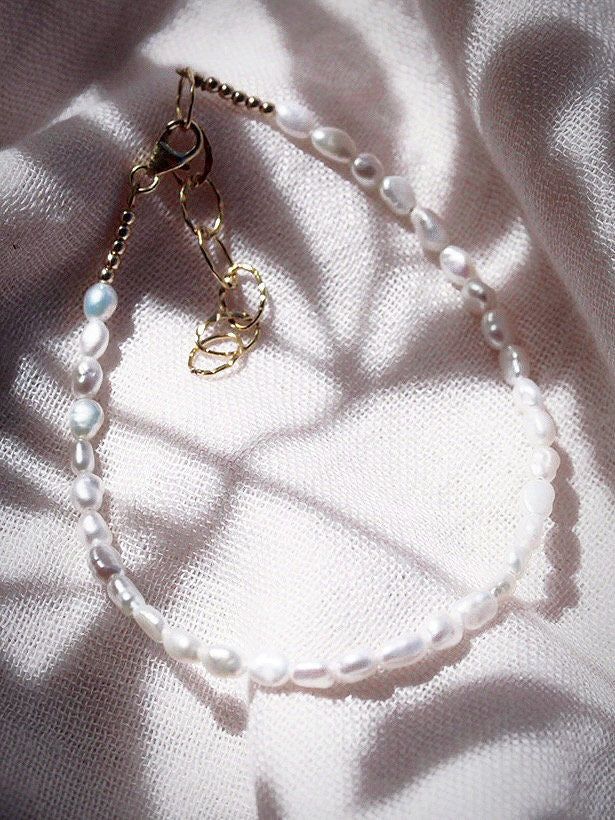 This beaded anklet features a collection of tiny white freshwater pearls to capture the enticement of Hawaii’s white sand beaches. Wear this gold pearl anklet alone or stacked for a classically elegant allure. ✦ DETAILS ✦✧ Name: Maile (MIE-leh) - vine.✧ Adjustable Length up to 10" Inches.✧ White 2-3mm Freshwater Pearls.✧ 14kt Gold Filled Components, Extender, and Clasp.✧ All Ke Aloha Jewelry pieces come packaged thoughtfully, beautifully, and ready for gift giving. Adjustable White Pearl Anklets, Delicate White Anklet As A Gift, Adjustable White Pearl Chain Anklet, White Anklets With Pearl Charm As Gift, Tiny Beads Pearl Bracelet, Adjustable Dainty Pearl Anklets, Gold Pearl Anklet With Pearl Charm, Elegant Adjustable Pearl Anklets, Elegant White Anklets With Pearl Chain