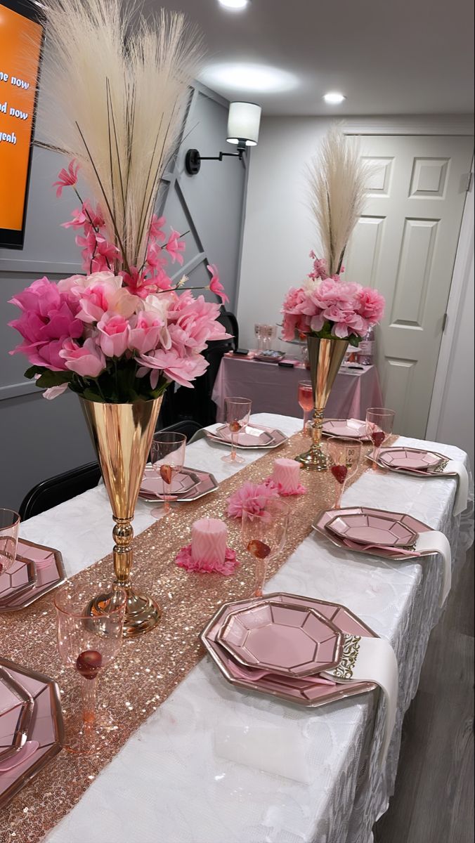 the table is set with pink and gold plates, silverware, and vases