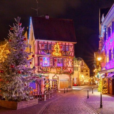 a street with christmas lights and decorations on the side of buildings in front of trees